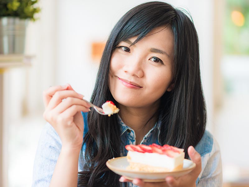 Portrait of young Asian pretty smiling woman eating cake